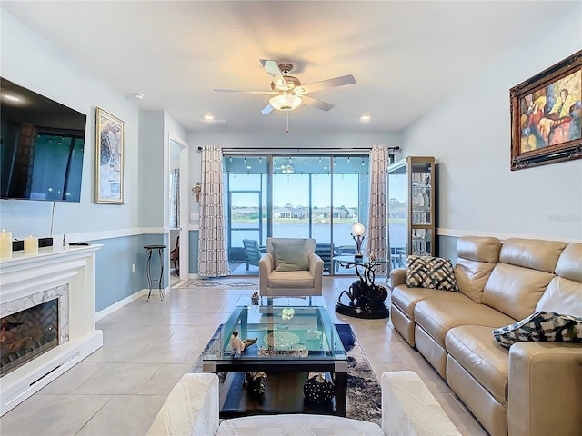 tiled living room with ceiling fan, a water view, and a premium fireplace