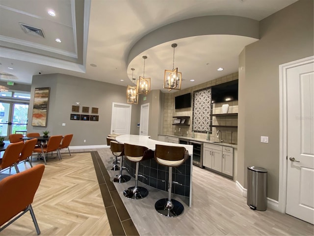 bar featuring tasteful backsplash, light parquet flooring, pendant lighting, sink, and beverage cooler