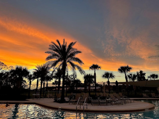 pool at dusk featuring a water view and a patio