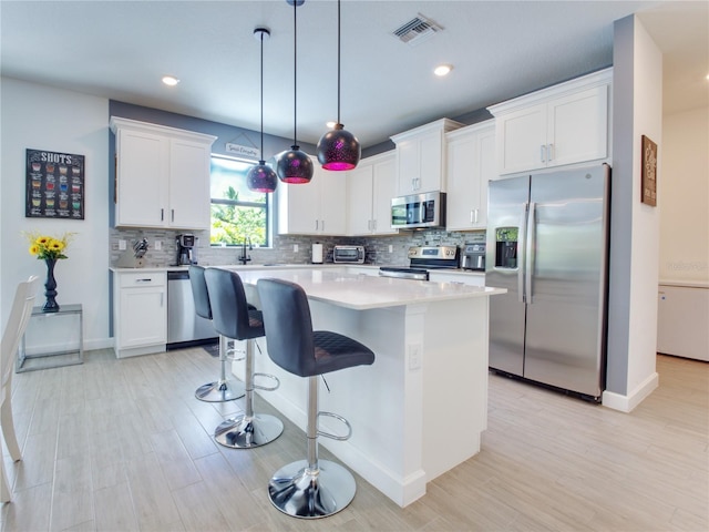 kitchen featuring pendant lighting, white cabinets, a center island, stainless steel appliances, and a breakfast bar area