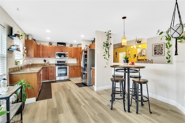 kitchen with light hardwood / wood-style floors, pendant lighting, sink, light stone countertops, and appliances with stainless steel finishes