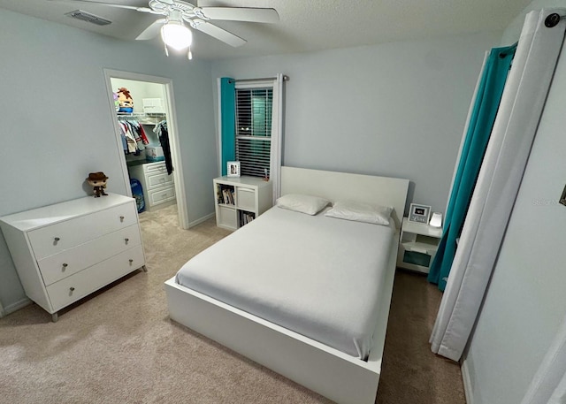 bedroom with ceiling fan, a walk in closet, a closet, and light colored carpet