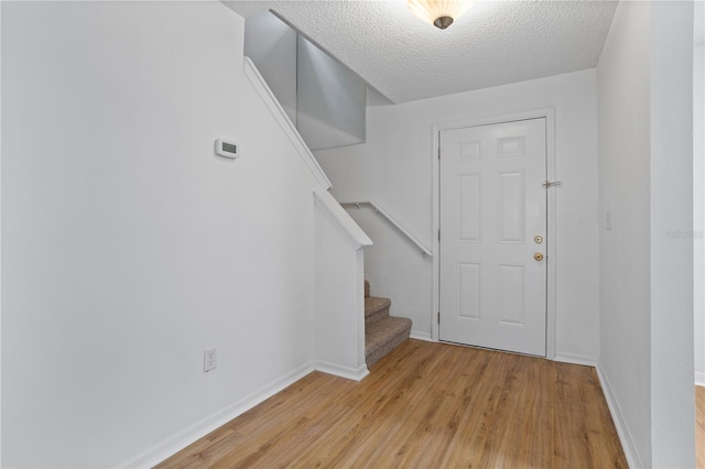 entryway with light wood-type flooring, baseboards, stairway, and a textured ceiling