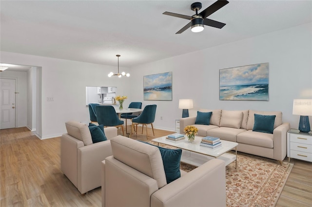 living room with ceiling fan with notable chandelier and light hardwood / wood-style flooring