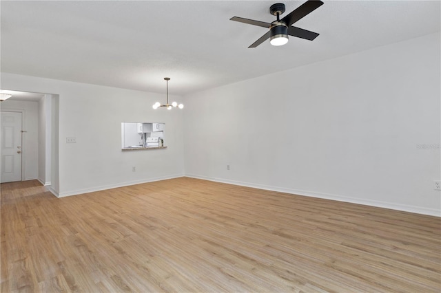 spare room featuring ceiling fan with notable chandelier, light wood-style flooring, and baseboards