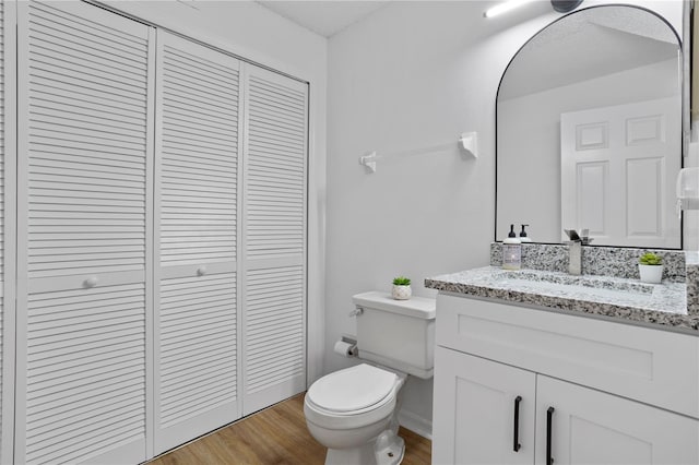 half bath with toilet, vanity, a closet, and wood finished floors