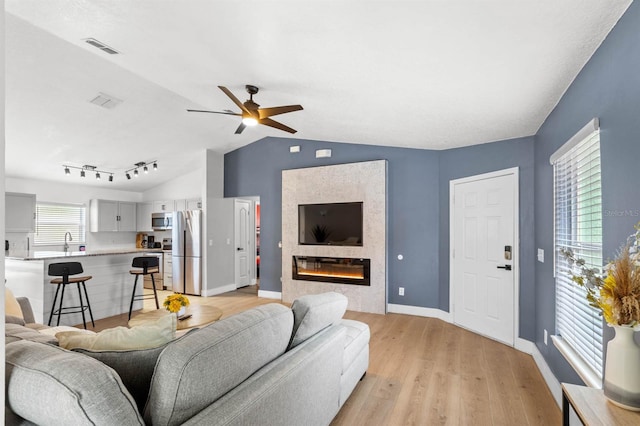 living room with light hardwood / wood-style flooring, ceiling fan, sink, rail lighting, and lofted ceiling