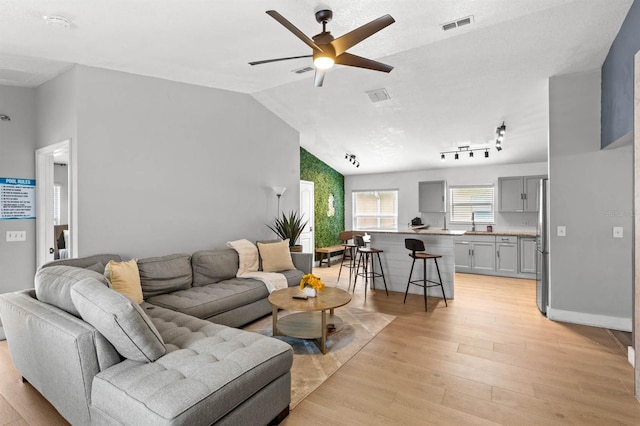 living room with ceiling fan, light hardwood / wood-style floors, and lofted ceiling