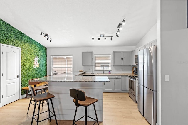 kitchen featuring a kitchen bar, sink, light hardwood / wood-style flooring, stainless steel appliances, and gray cabinets