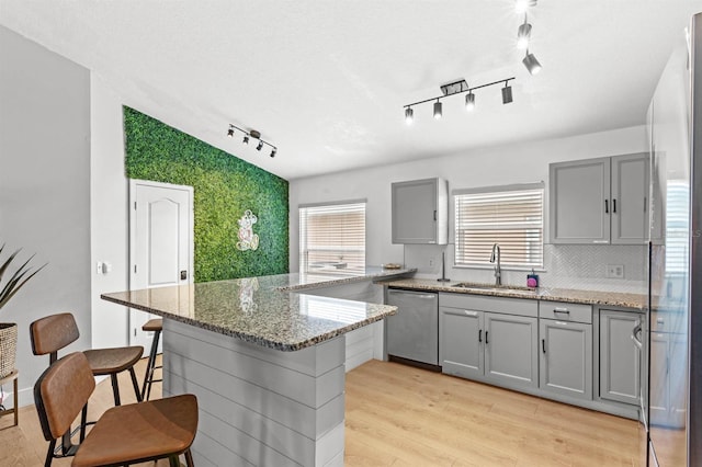 kitchen with a kitchen bar, light stone countertops, gray cabinetry, sink, and stainless steel appliances