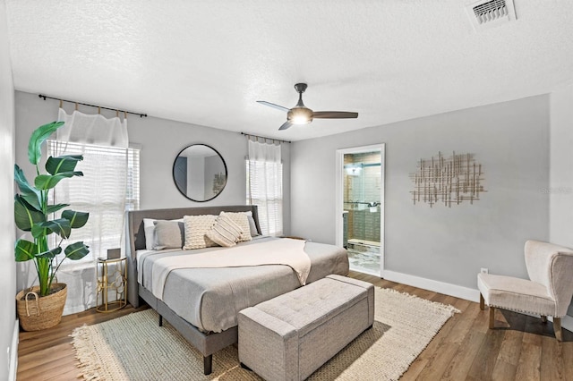 bedroom with ceiling fan, hardwood / wood-style floors, a textured ceiling, and ensuite bath