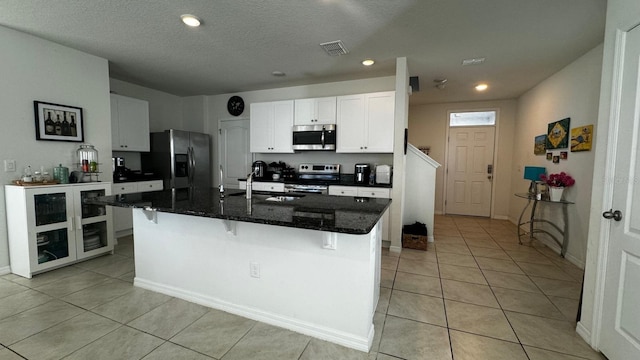 kitchen with dark stone countertops, sink, an island with sink, stainless steel appliances, and white cabinets