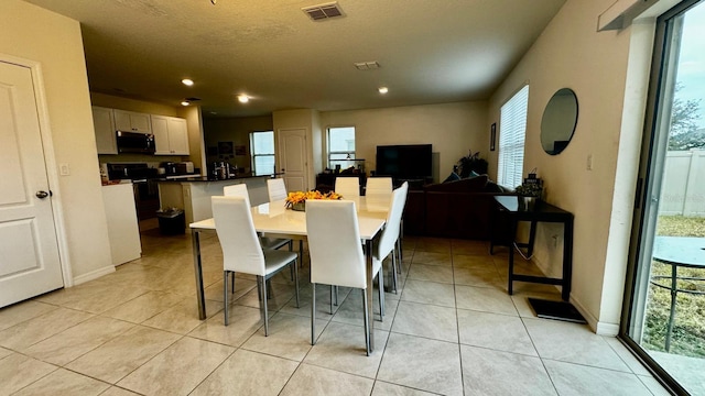 dining space with a textured ceiling, light tile patterned floors, and a healthy amount of sunlight