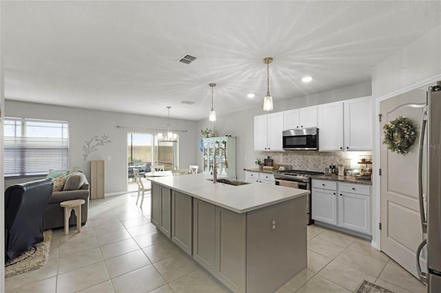 kitchen with decorative light fixtures, white cabinets, a kitchen island with sink, and appliances with stainless steel finishes