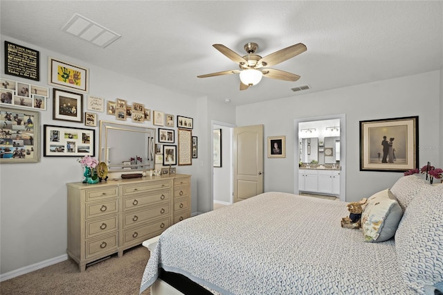 bedroom with ceiling fan, connected bathroom, light colored carpet, and a textured ceiling