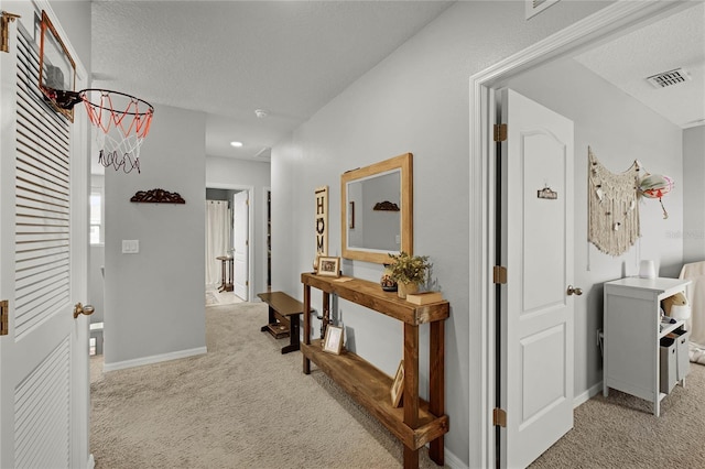 hallway with light carpet and a textured ceiling