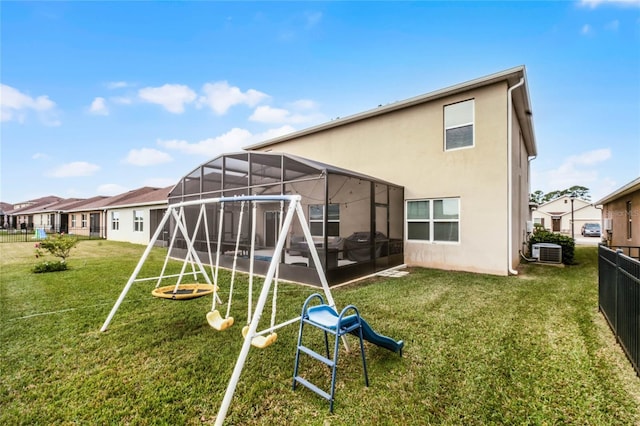 rear view of house featuring a playground, cooling unit, glass enclosure, and a lawn