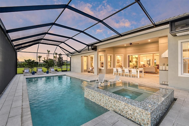 pool at dusk with a lanai, ceiling fan, a patio area, outdoor lounge area, and an in ground hot tub