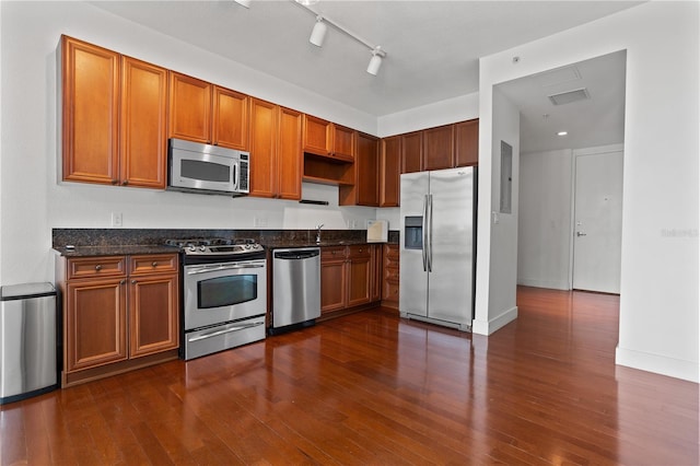 kitchen with rail lighting, dark hardwood / wood-style flooring, stainless steel appliances, and dark stone countertops