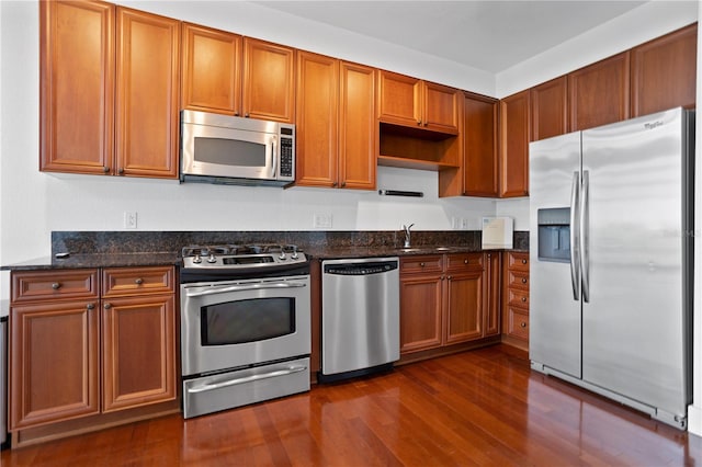 kitchen with sink, dark hardwood / wood-style floors, stainless steel appliances, and dark stone countertops