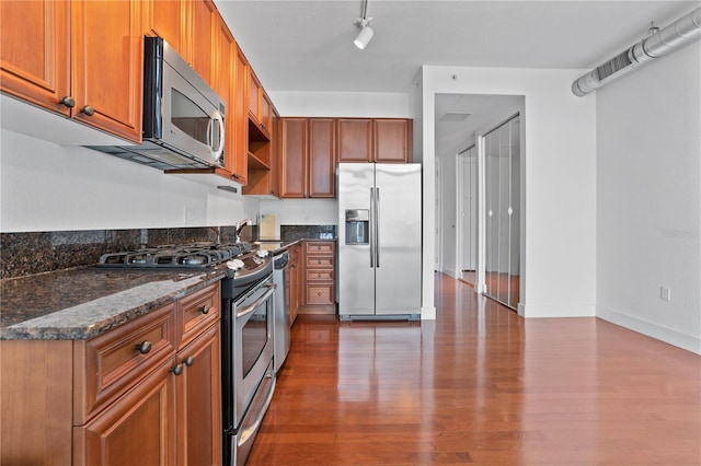 kitchen with appliances with stainless steel finishes, dark hardwood / wood-style flooring, dark stone countertops, rail lighting, and sink