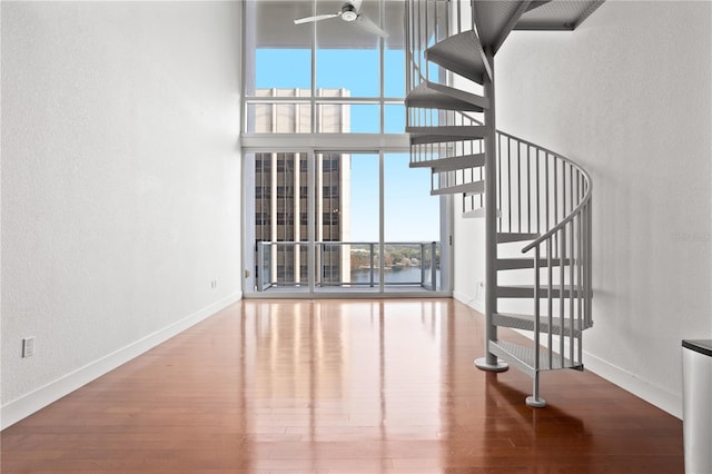 interior space with ceiling fan, a water view, hardwood / wood-style floors, and expansive windows