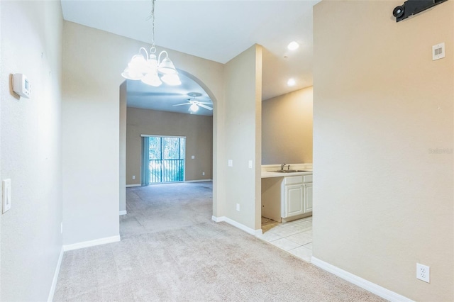 unfurnished dining area featuring light colored carpet, sink, and ceiling fan with notable chandelier