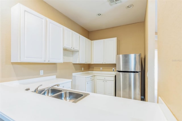 kitchen with stainless steel fridge, sink, and white cabinetry