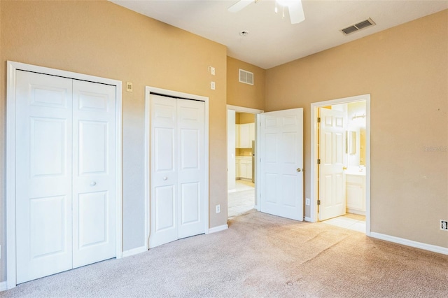 unfurnished bedroom featuring ceiling fan, light colored carpet, ensuite bath, and multiple closets