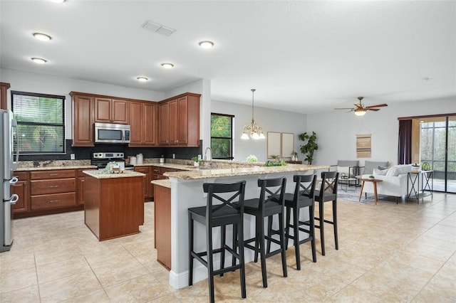 kitchen with a breakfast bar area, a kitchen island, pendant lighting, stainless steel appliances, and light stone countertops