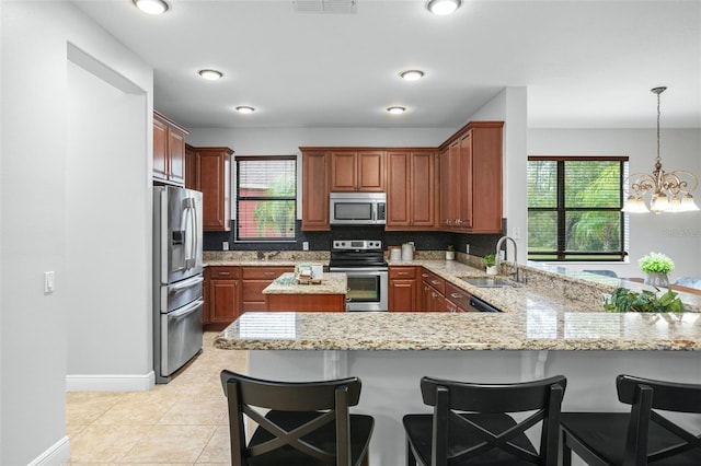 kitchen featuring appliances with stainless steel finishes, hanging light fixtures, sink, kitchen peninsula, and light stone counters