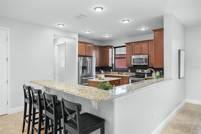 kitchen with light stone countertops, a breakfast bar, appliances with stainless steel finishes, and kitchen peninsula