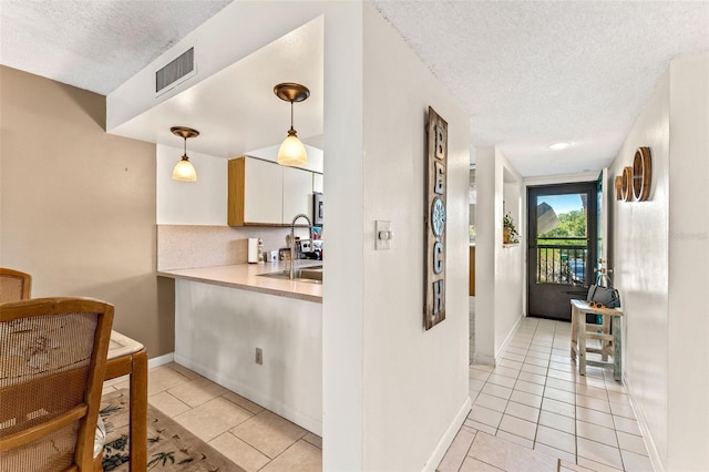 kitchen featuring pendant lighting, white cabinetry, light tile patterned flooring, and a textured ceiling