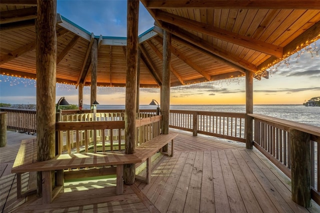 deck at dusk featuring a gazebo, a water view, and a view of the beach