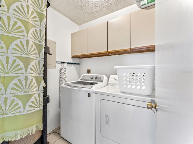 clothes washing area with light tile patterned floors, washing machine and clothes dryer, cabinets, and a textured ceiling