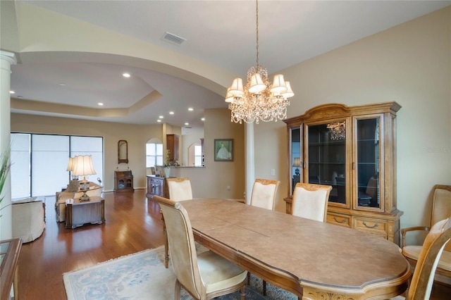 dining room with a raised ceiling, an inviting chandelier, and dark wood-type flooring