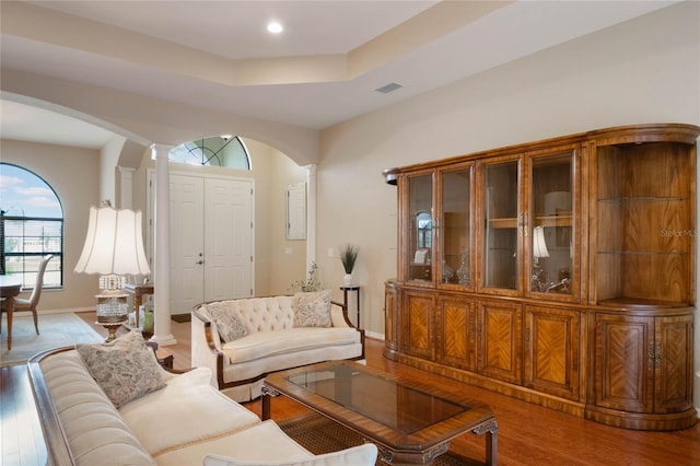 living room with hardwood / wood-style floors, a raised ceiling, and ornate columns