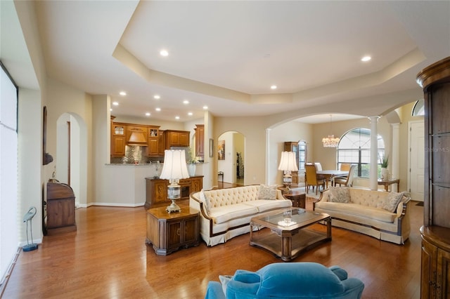 living room with light hardwood / wood-style floors, a tray ceiling, and ornate columns