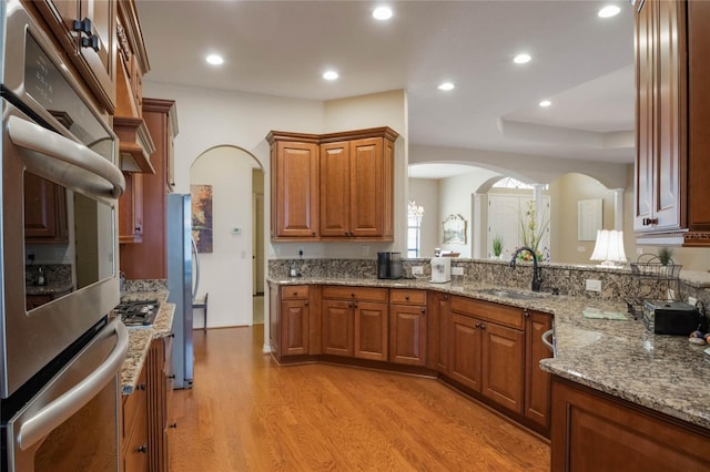 kitchen featuring sink, stainless steel appliances, light stone countertops, and light wood-type flooring