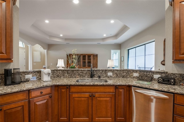 kitchen with light stone countertops, decorative columns, dishwasher, sink, and a tray ceiling