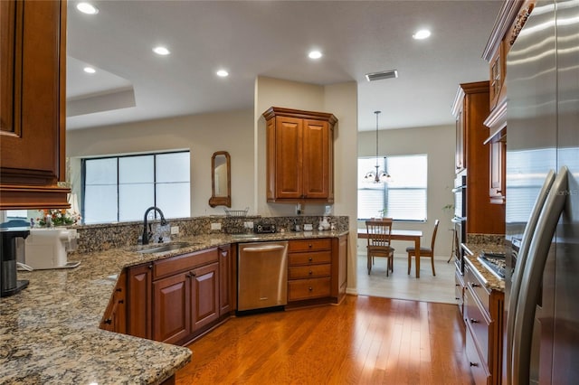 kitchen featuring appliances with stainless steel finishes, decorative light fixtures, dark wood-type flooring, sink, and light stone counters