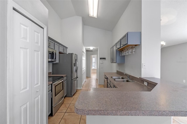 kitchen featuring stainless steel appliances, sink, kitchen peninsula, vaulted ceiling, and light tile patterned floors