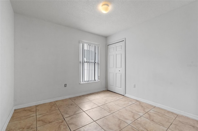 spare room with a textured ceiling and light tile patterned flooring