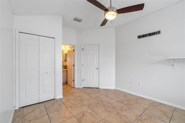 unfurnished bedroom featuring ceiling fan, vaulted ceiling, ensuite bath, light tile patterned floors, and a closet