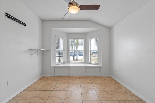 empty room with lofted ceiling, ceiling fan, light tile patterned flooring, and a textured ceiling