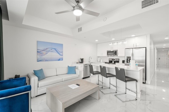 living room with ceiling fan, a raised ceiling, and sink