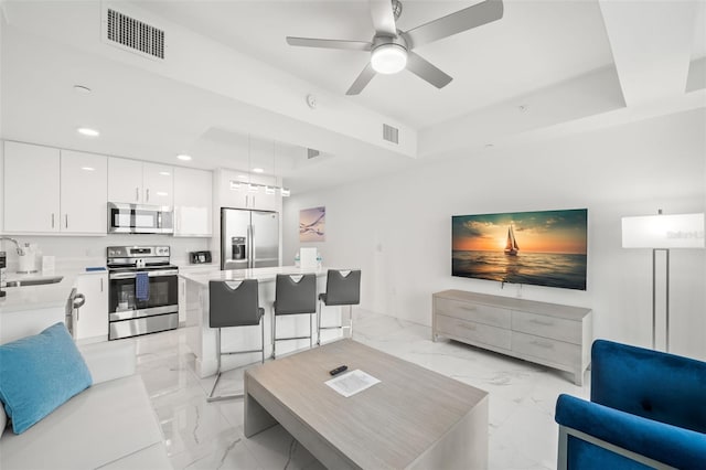 living room with a raised ceiling, ceiling fan, and sink