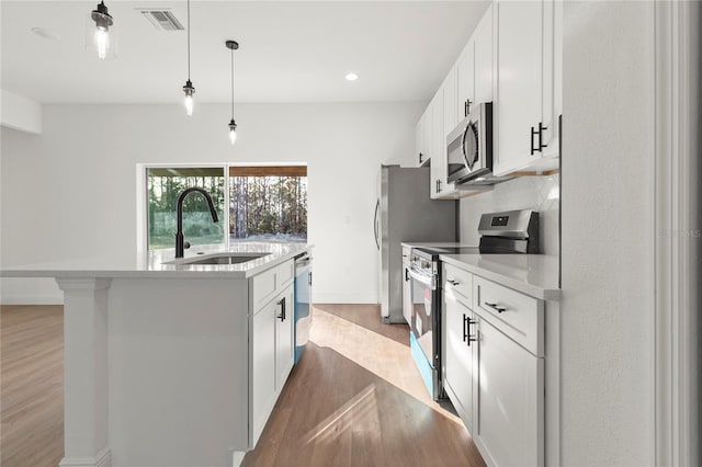 kitchen featuring white cabinets, an island with sink, appliances with stainless steel finishes, light countertops, and a sink