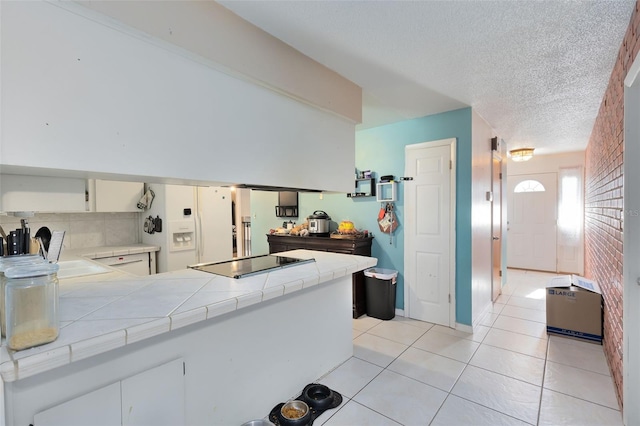 kitchen with tile countertops, kitchen peninsula, black electric cooktop, brick wall, and white cabinets