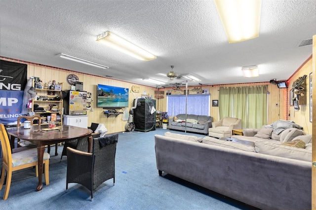 carpeted living room with ceiling fan, a textured ceiling, and wood walls